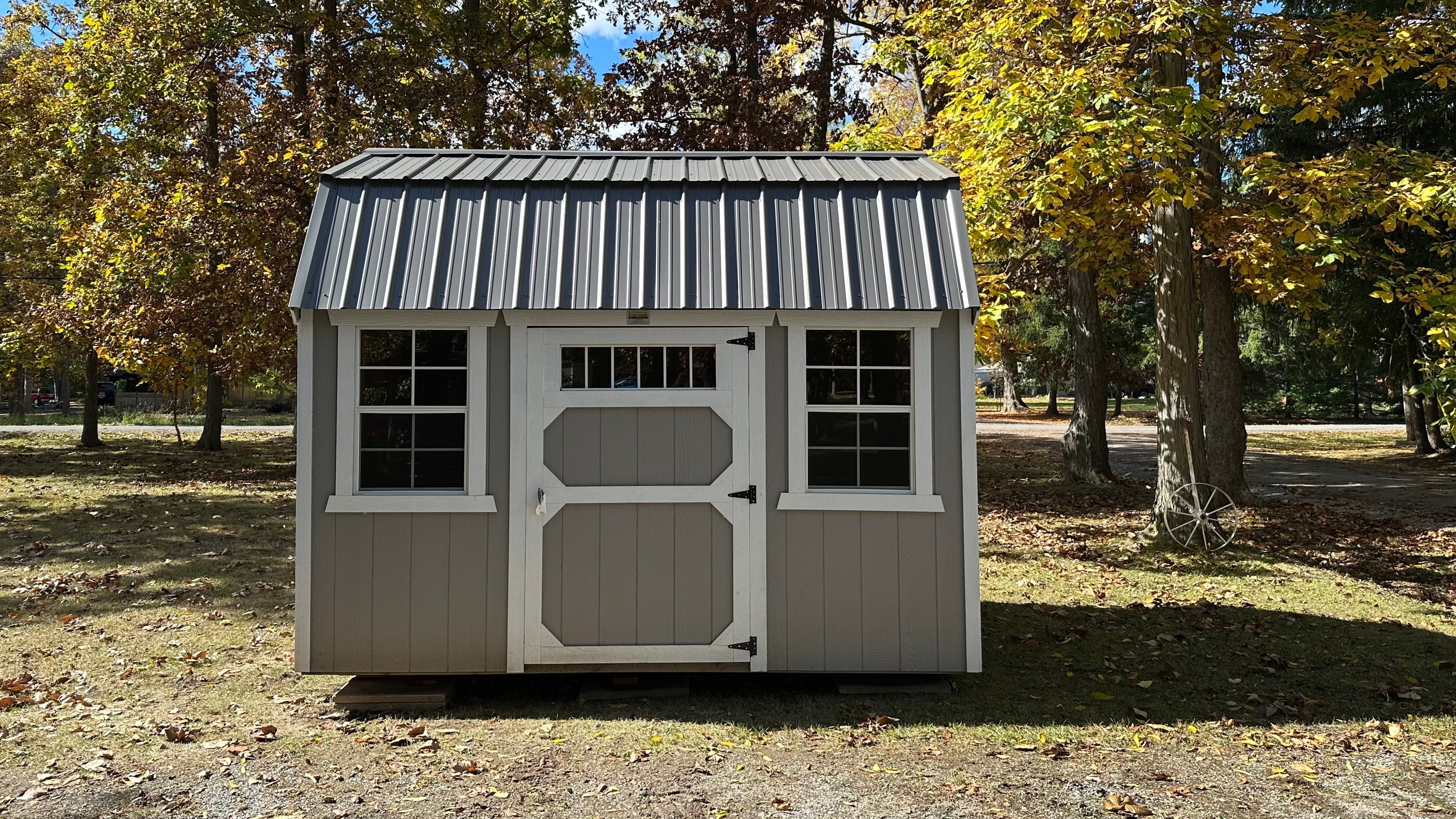 Small storage shed with a metal roof in a park-like setting with trees and grass.